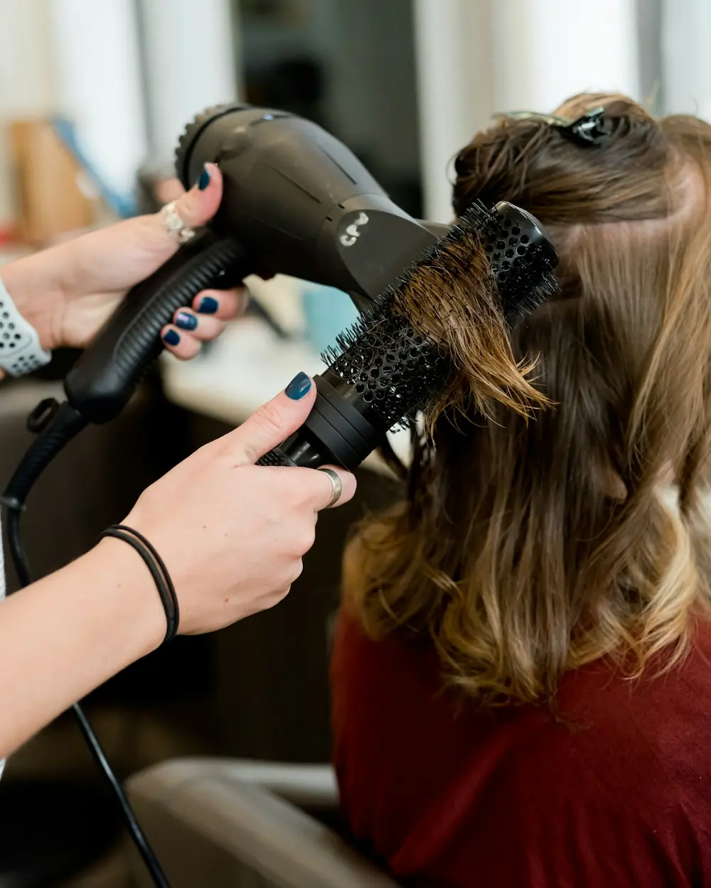 A stylist blow-drying shoulder-length hair over a round brush